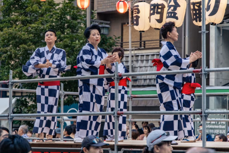 Dancers in checkered yukatas perform on a stage during the Kaminarimon Bon Odori 2025 festival.