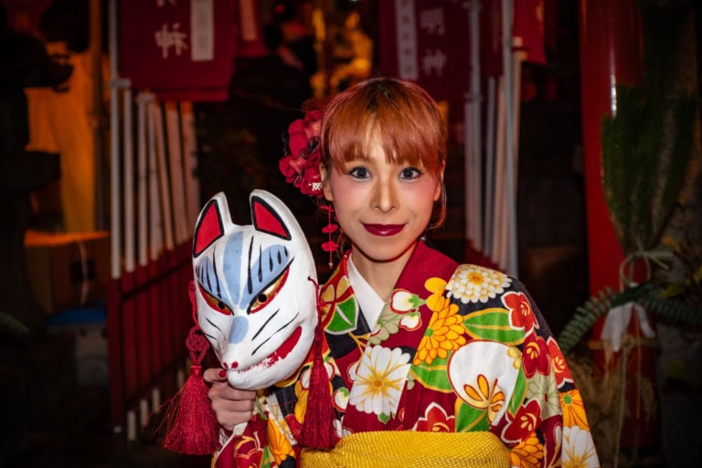 Woman in a floral kimono holding a kitsune mask at the Oji Fox Parade night festival.