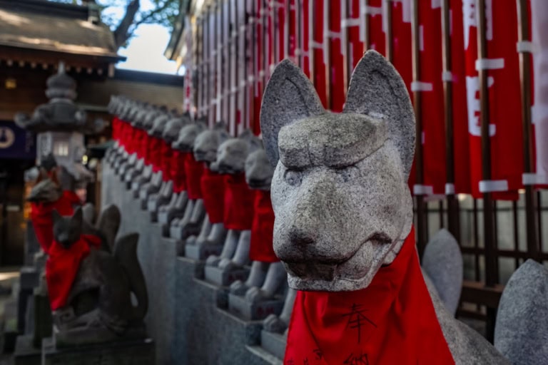 Stone fox statues wearing red bibs at Toyokawa Inari Tokyo Betsuin shrine.