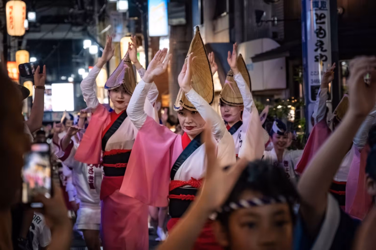 Women in woven hats and pink attire dance at the Shimokitazawa Awa Odori 2024 street festival at night.