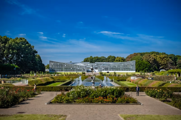 Manicured gardens and fountains lead to a large glass conservatory under a clear sky at Jindai Botanical Gardens.