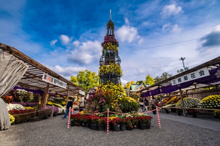Tall chrysanthemum tower at the Kameido Tenjin Chrysanthemum Festival surrounded by garden displays and visitors.