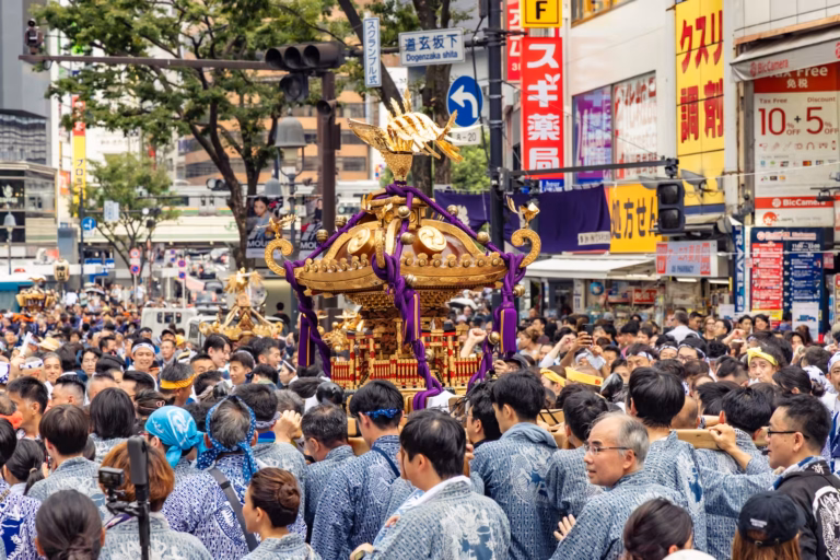 Crowd in patterned coats carries a golden mikoshi shrine through Shibuya for the Konno Hachimangu Festival.