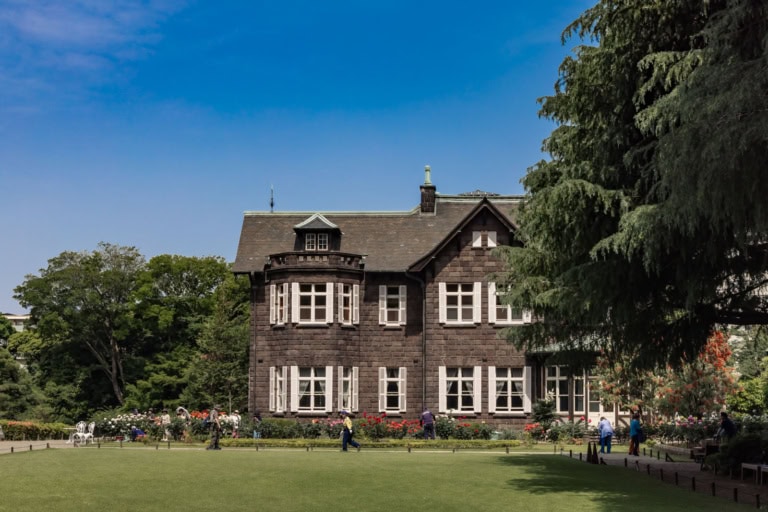 Josiah Conder’s Western-style stone mansion at Kyu-Furukawa Gardens on a green lawn and rose beds under a cloudless sky.