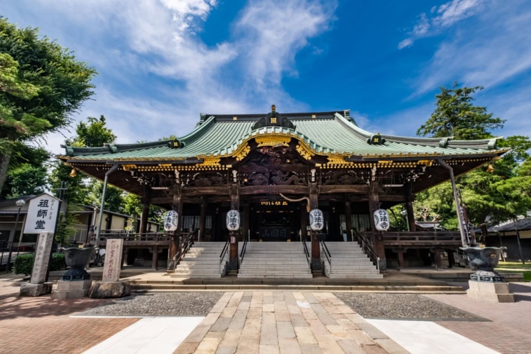 Front view of Myohoji Temple with detailed wood carvings and white lanterns under a bright blue sky.