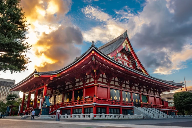 Sensoji Temple's red architecture and peaked roof set against a dramatic sunset sky with orange and blue clouds.