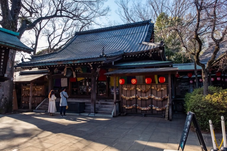 Traditional temple in Todoroki Valley with red lanterns, wooden prayer plaques, and visitors in the sunny courtyard.