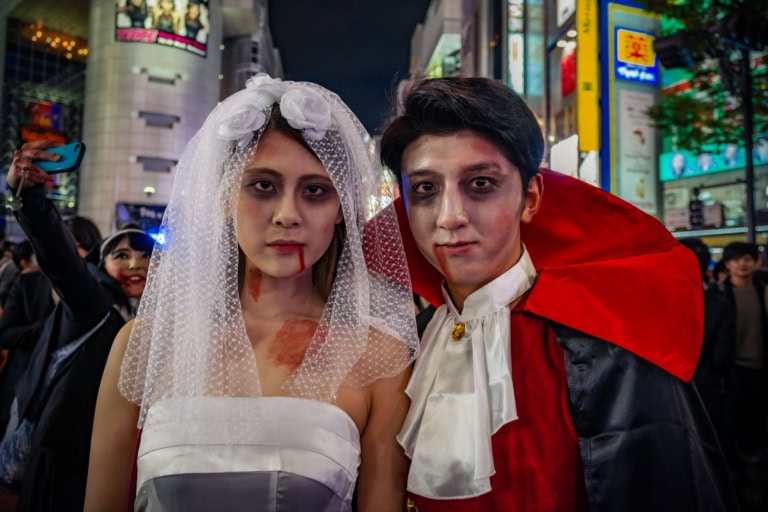 A couple in eerie bridal and vampire costumes with fake blood at Shibuya Halloween 2017 near Shibuya 109.
