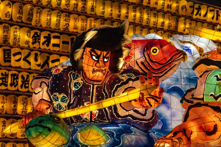 Nebuta float of a warrior and red fish, glowing brightly against a background of illuminated yellow lanterns.