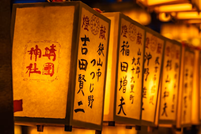 A row of square paper lanterns with Japanese calligraphy glows warmly, with the background lanterns softly blurred.