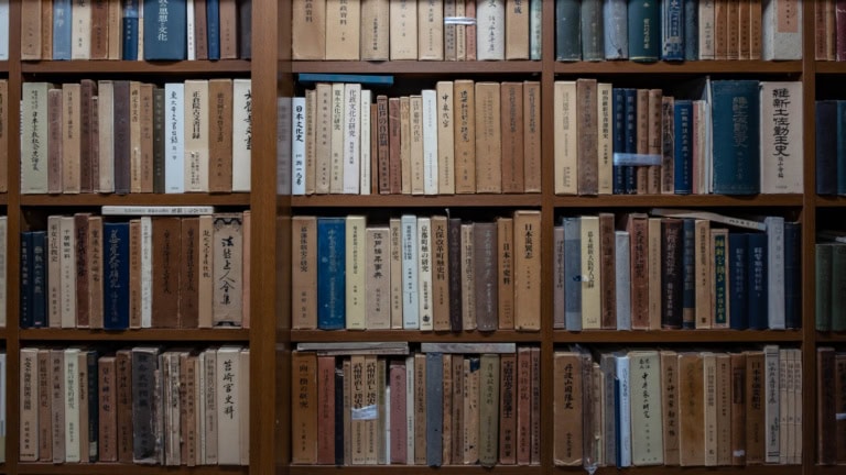 Wooden bookshelves filled with rows of rare Japanese books with text on their spines at Sarashobo.