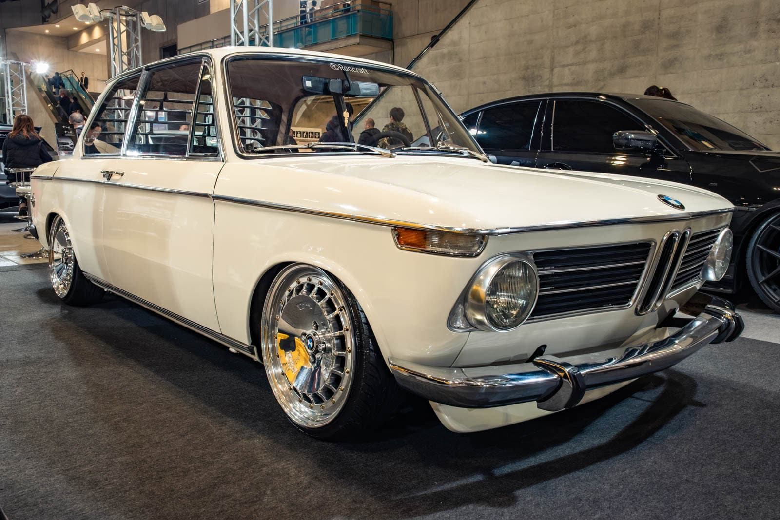 BMW E10 at Tokyo Auto Salon 2020, shown with background architectural features and a dark car.