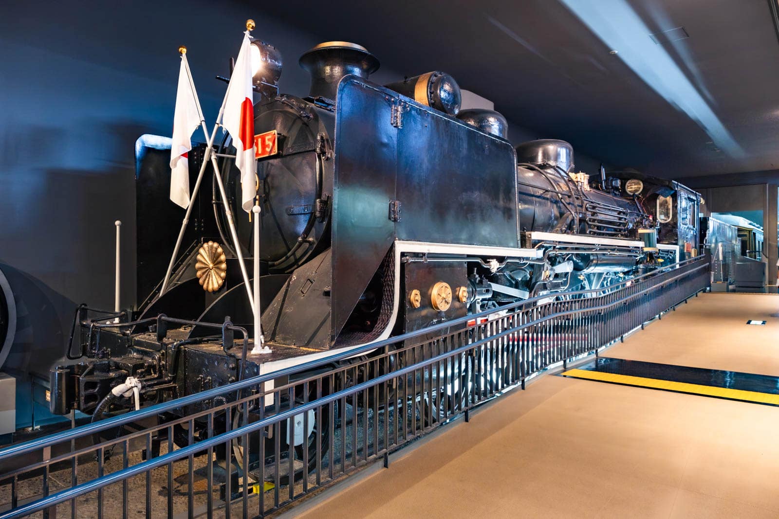 Black Class C51 steam locomotive on display indoors behind a railing, decorated with two Japanese flags.