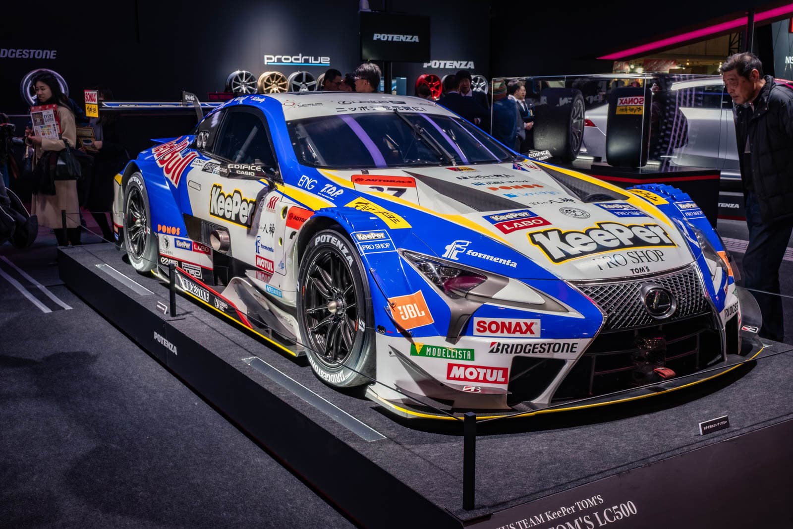 Lexus LC500 GT racecar at Tokyo Auto Salon 2020, displayed on a platform with background signs and attendees.