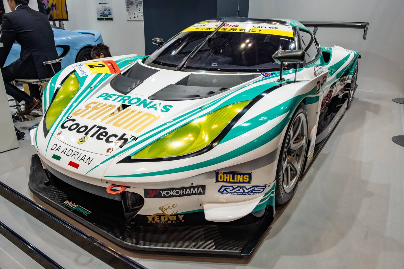 Lotus Evora racecar at Tokyo Auto Salon 2020, shown with a background display and seated attendee.