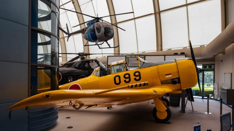 North American T-6 Texan monoplane displayed inside the Tokorozawa Aviation Museum, with a helicopter suspended above.
