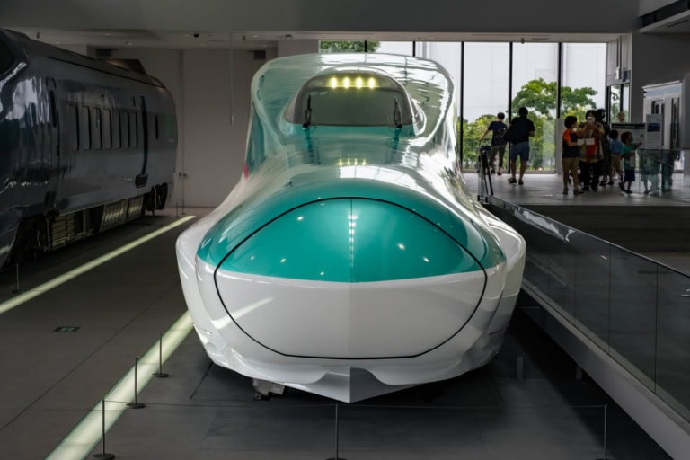 Green and white Series E5 Shinkansen bullet train on display indoors with visitors standing nearby.