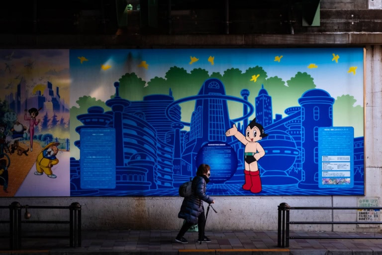 A person walks past a large street mural featuring Astro Boy in front of a blue futuristic cityscape.