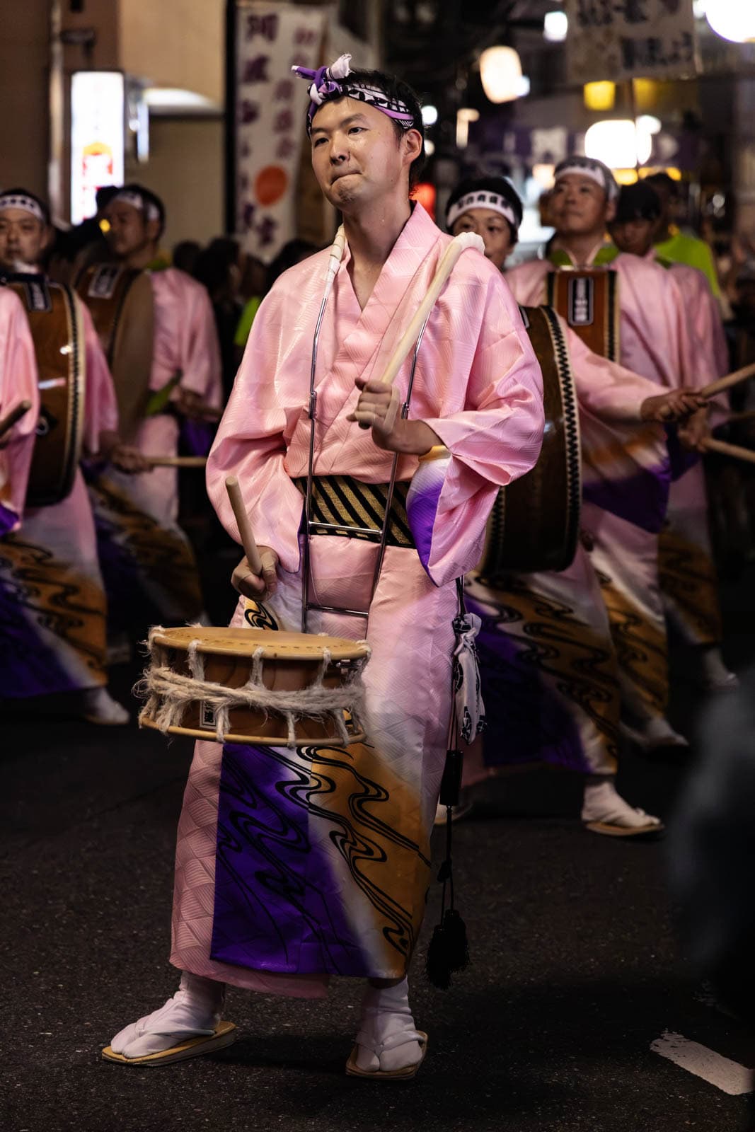 A drummer in a pink kimono plays a small drum during a nighttime street festival in Tokyo.