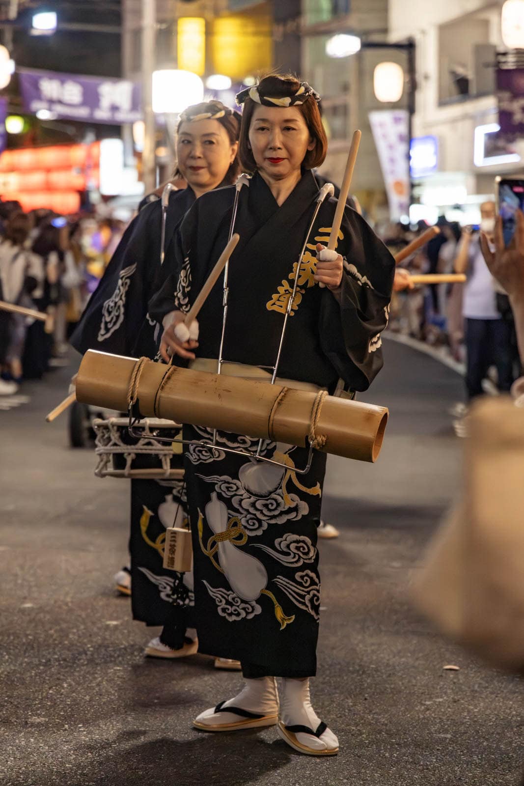Performers in black kimonos play bamboo instruments and drums during a nighttime street festival in Tokyo.