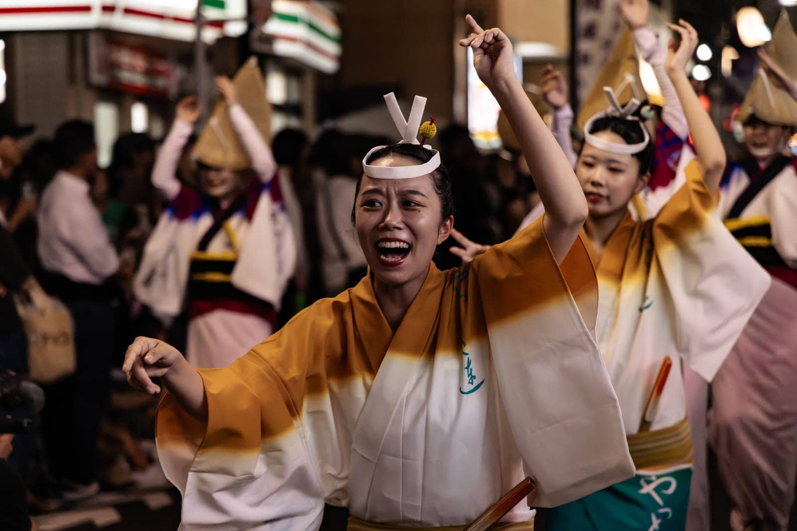A smiling dancer in a yellow and white happi coat performs at the Hatsudai Awa Odori.