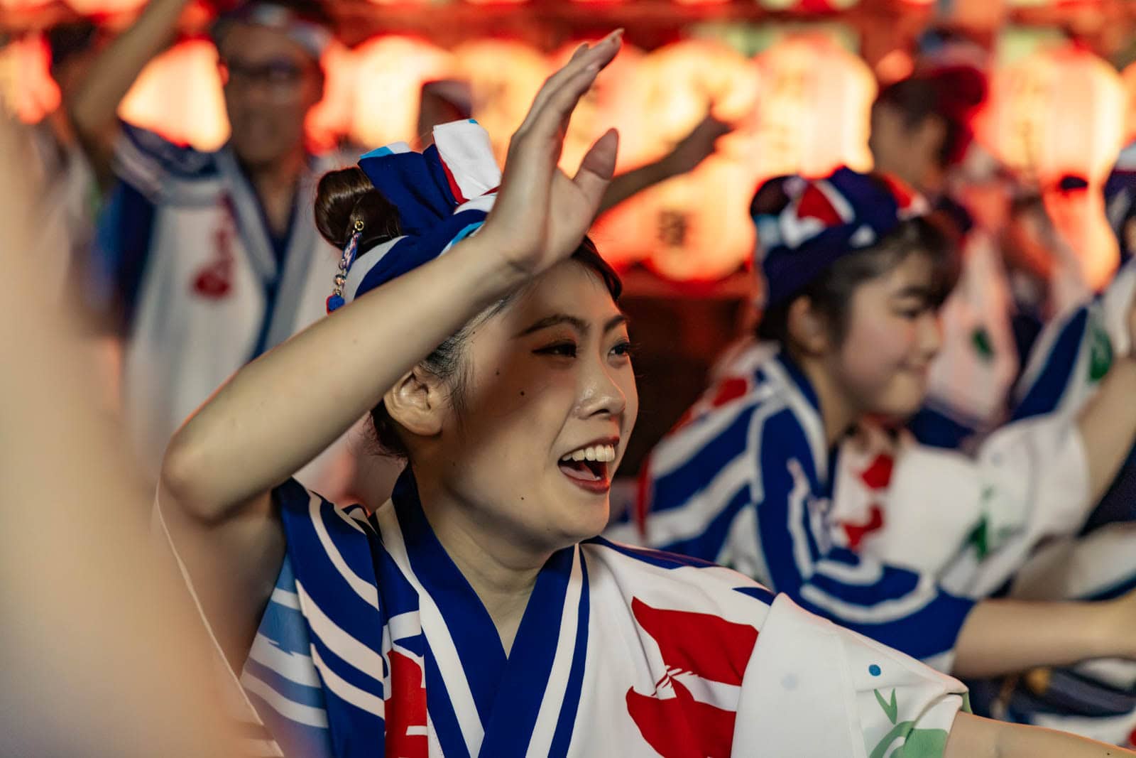 A smiling dancer in white, blue, and red attire raises a hand during a street festival in Tokyo.
