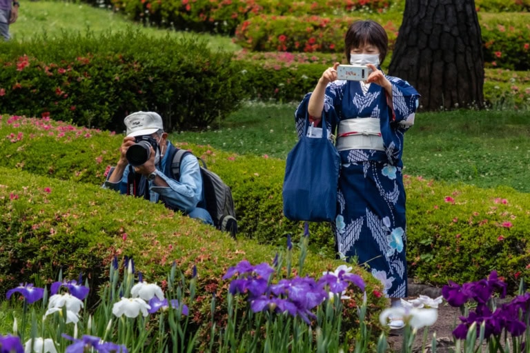 Woman in a blue kimono taking photos with a smartphone and a photographer with a camera at the Imperial Palace East Gardens.