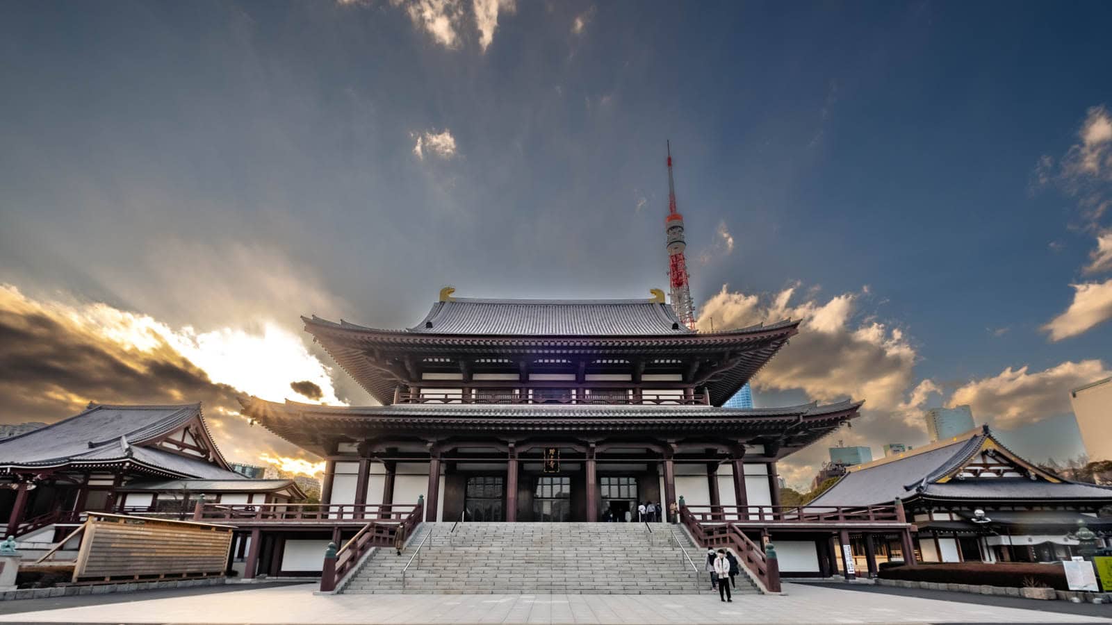 Zojoji Temple's main hall stands prominently with a large staircase, viewed against a dramatic cloudy sky and the Tokyo Tower.