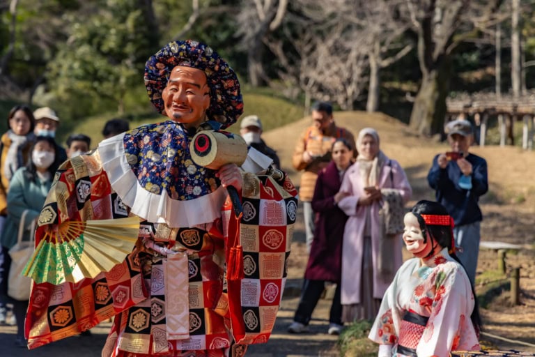 Koishikawa Korakuen Gardens Edo Sato Kagura performance: Shinto dancers wearing traditional masks and costumes on an outdoor stage.