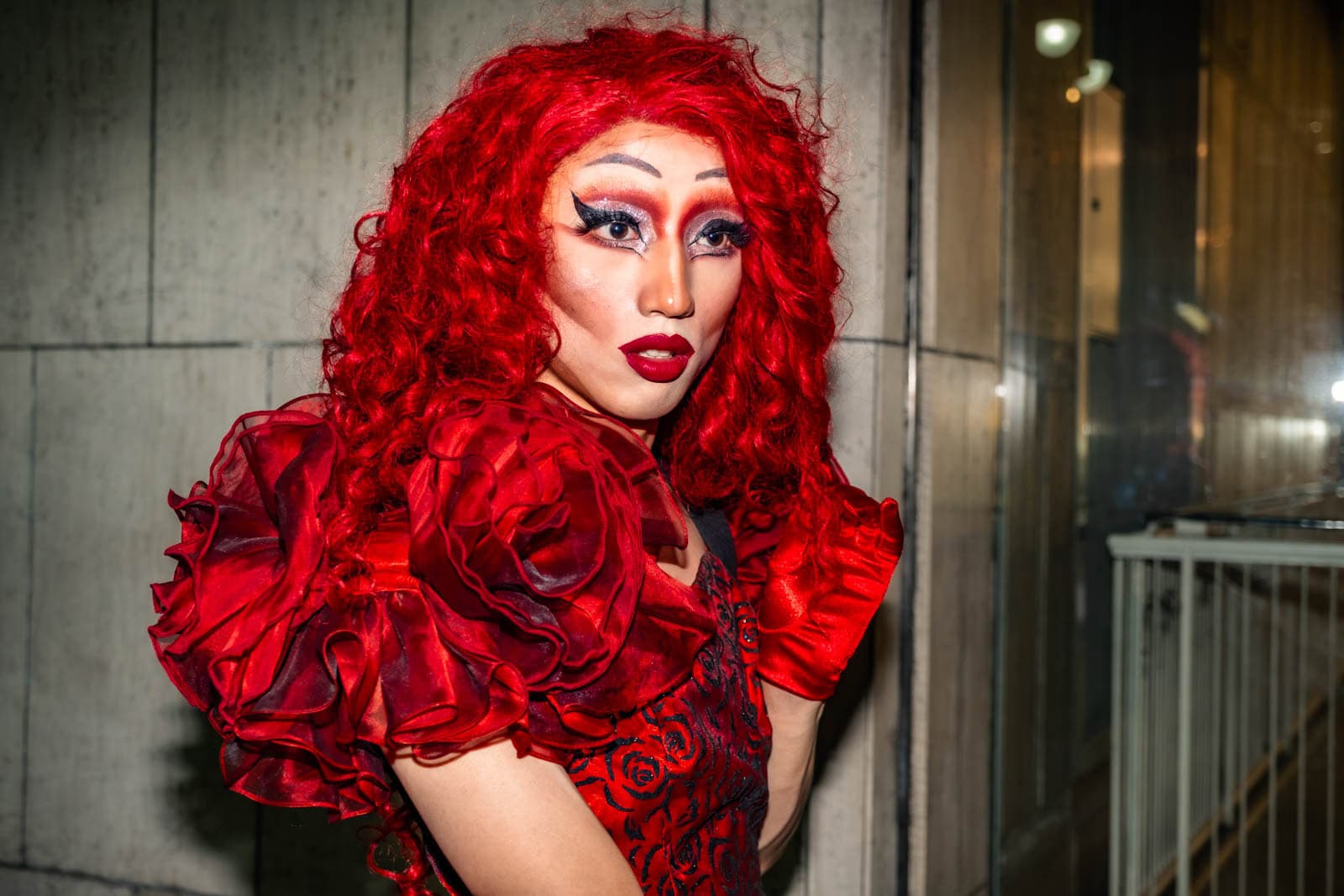 Shibuya drag queen wearing a red wig, heavy makeup, and ruffled dress during Halloween at night.