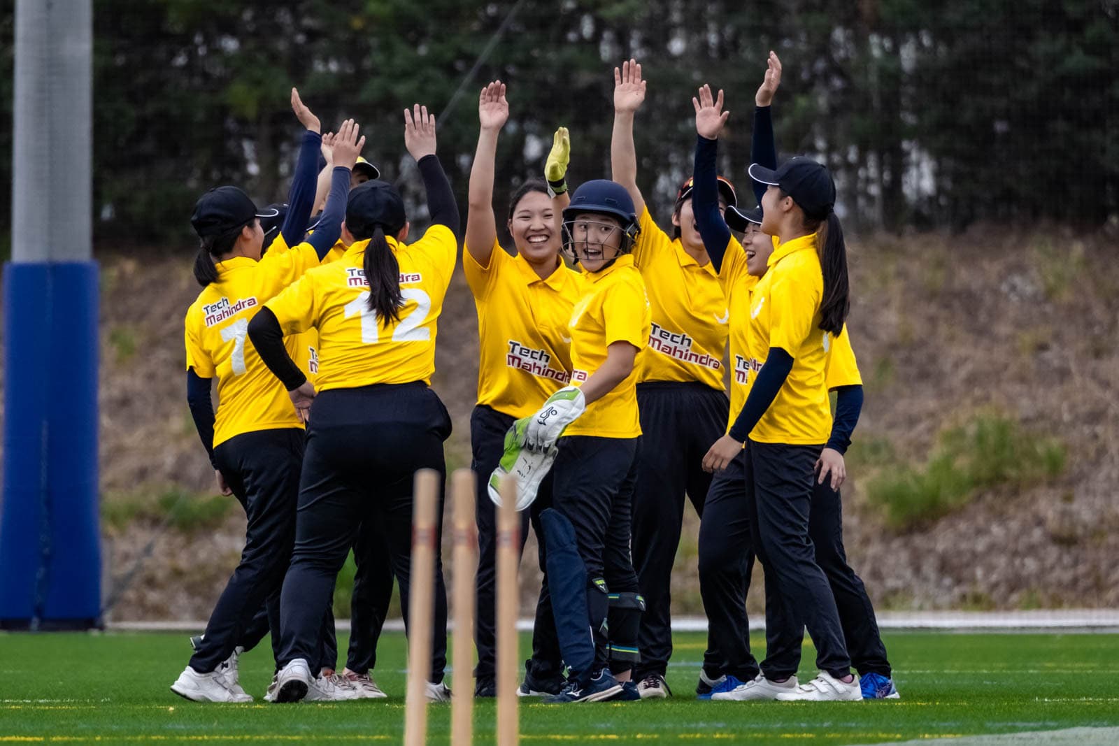 A Japanese women's cricket team members high-fiving in celebration during a Japan Cricket Association game.