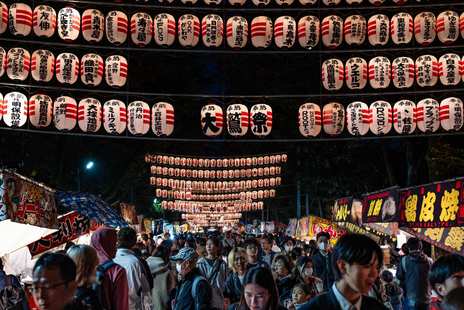 Rows of red and white chochin lanterns illuminate a crowd at Okunitama Shrine during the Tori-no-Ichi festival.