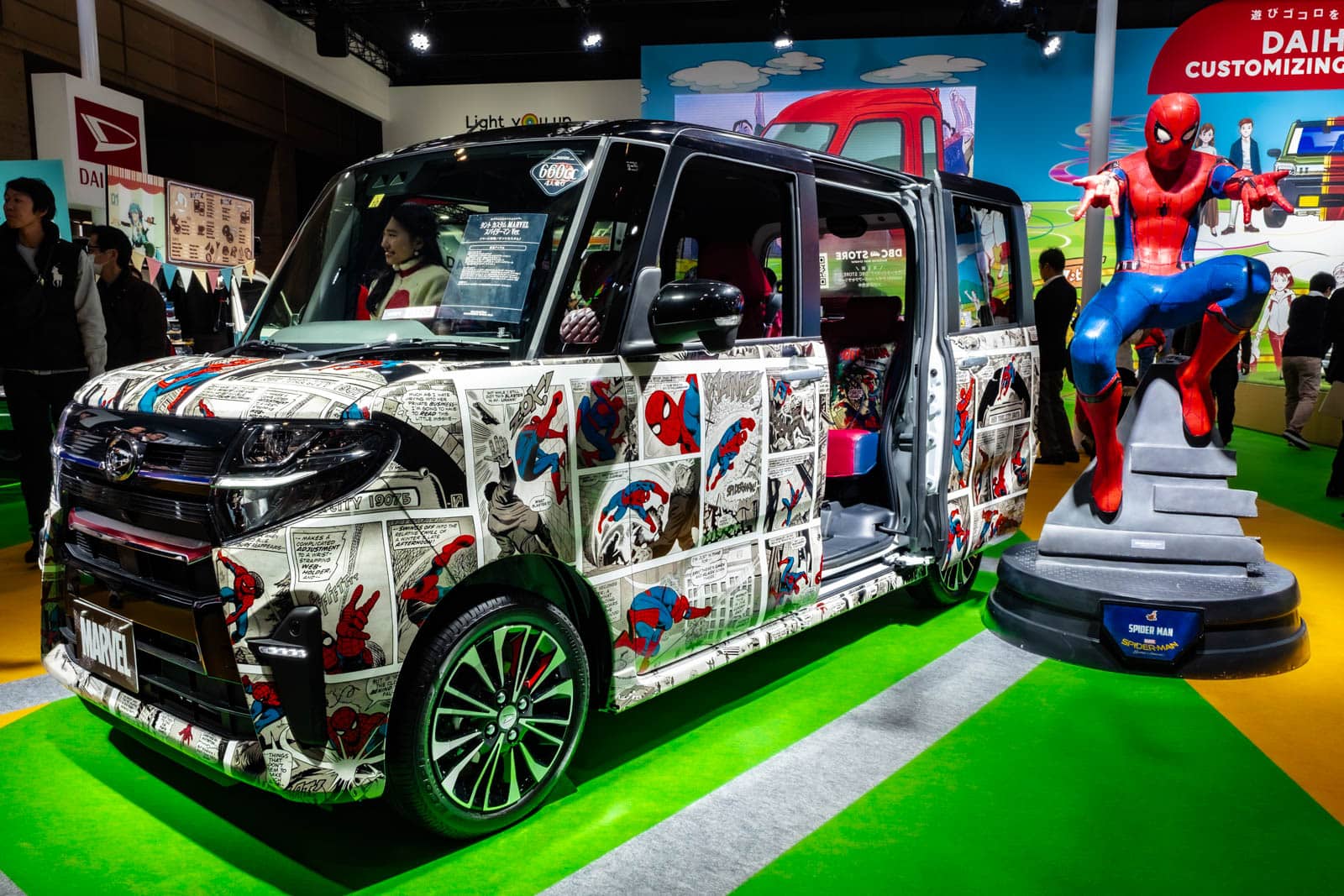 Spider-Man comic-wrapped Daihatsu van on display next to a life-size Spider-Man statue at Tokyo Auto Salon.