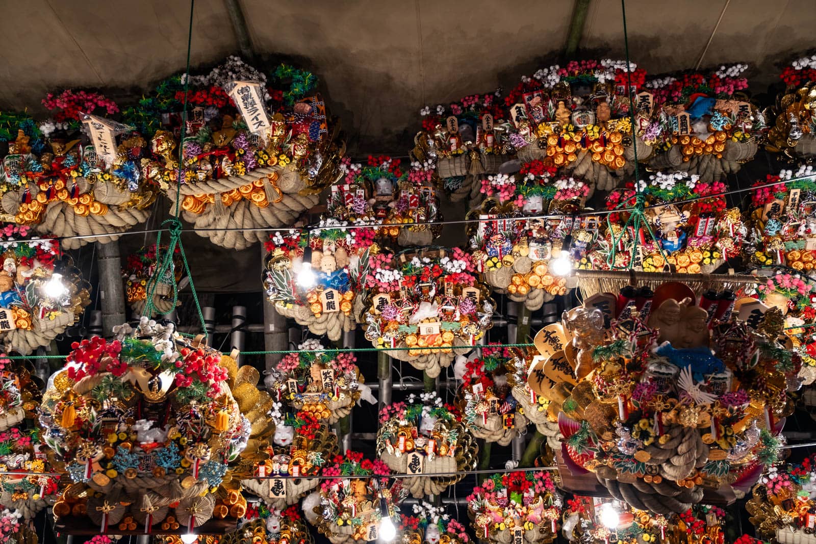 Kumade rakes hung for sale at Okunitama Shrine during the Tori-no-Ichi festival, with festival stalls in the background.