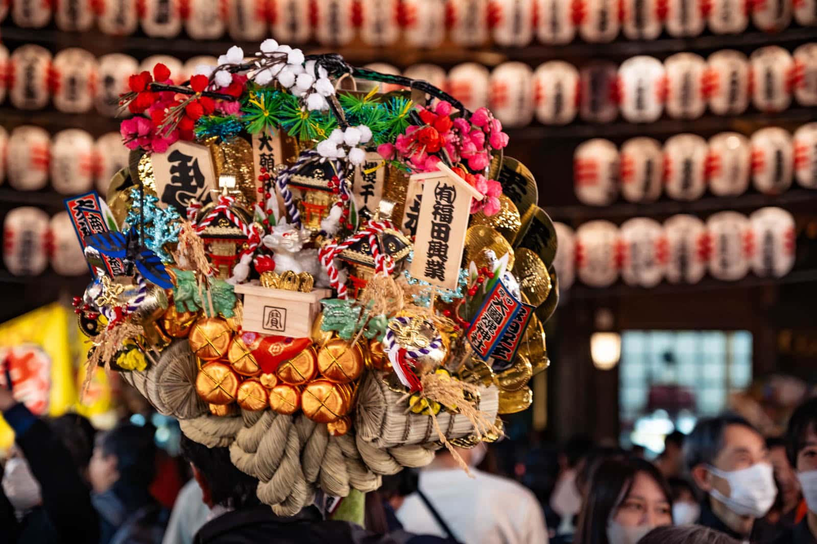 A decorated good luck rake at Okunitama Shrine during the Tori-no-Ichi festival, with rows of lanterns in the background.