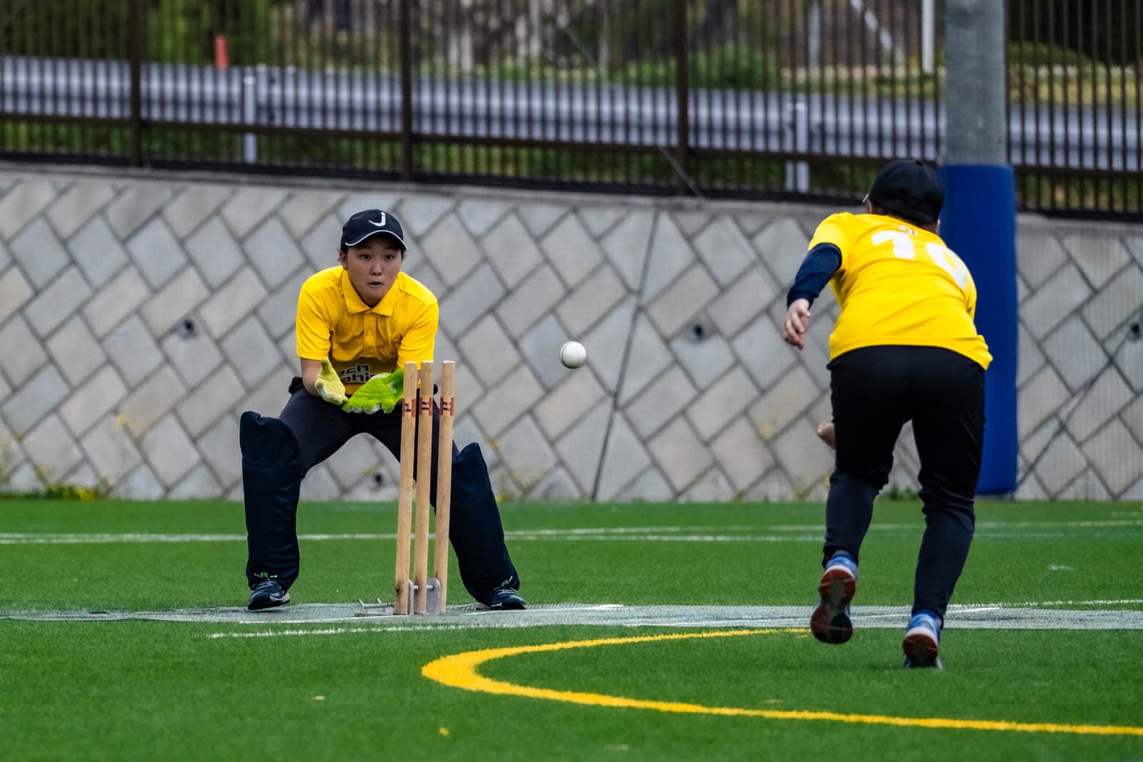A Japanese wicketkeeper prepares to catch the ball behind the stumps during a women's J-Bash cricket match.